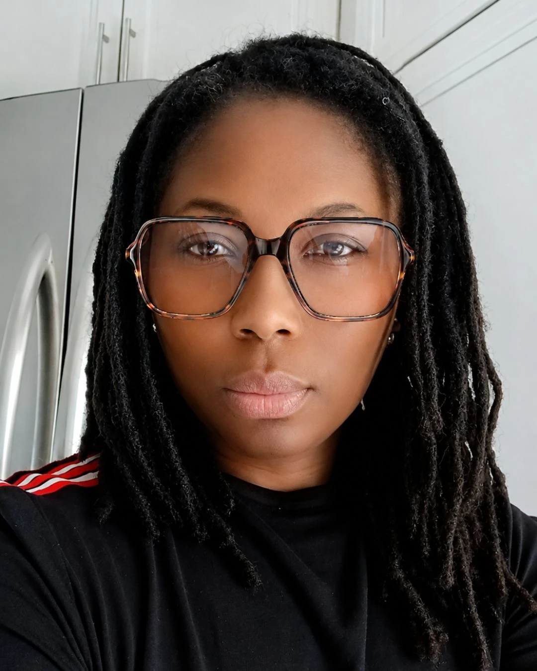 Afua, the loctician behind Sankofa Locks, looking straight at the camera, wearing glasses with her own locs falling past her shoulders
