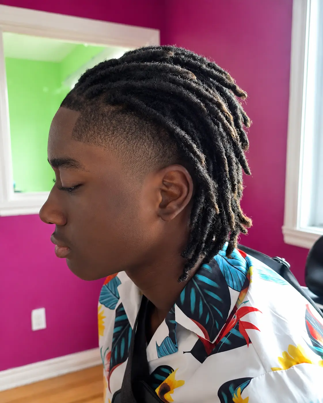 Side profile of a male client with locs on top and the sides tapered short, the loc ends lightened to honey